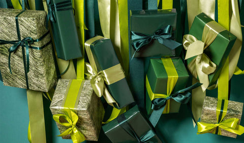 Gifts wrapped in different green gift wrappers hanging by green ribbons against a curtain of ribbons in different shades of green