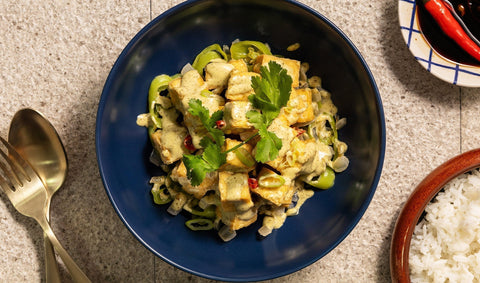A photo of sisig tofu in a blue bowl at the center, gold spoon and fork, white rice, and red peppers on the side