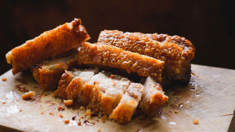 An image of a golden-brown, crispy pork belly, sliced and arranged on a wooden chopping board.