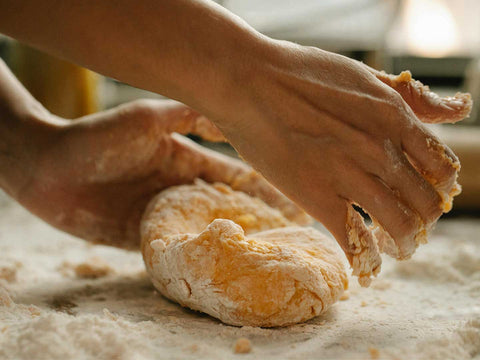 A close-up of hands kneading dough on a floured surface made by hand.