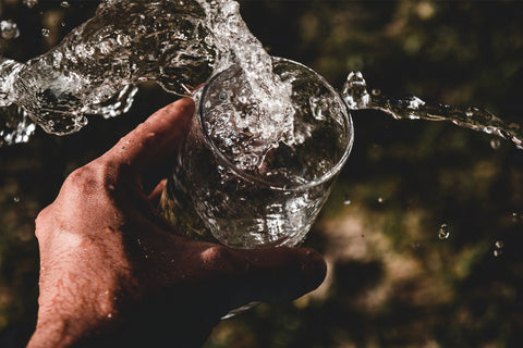 Water pouring into and splashing out of a glass of water held by a hand