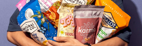 A man wearing a dark blue shirt holding several bags of snacks and chips in his arms