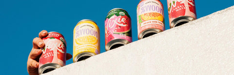 Swoon and Nixie canned drinks lined up on a white ledge with a hand holding one can