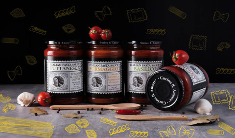 Jars of pasta sauces surrounded by cherry tomatoes, garlic cloves, seasonings, and wooden spoons on a grey tabletop, with illustrations of pasta shapes in the background