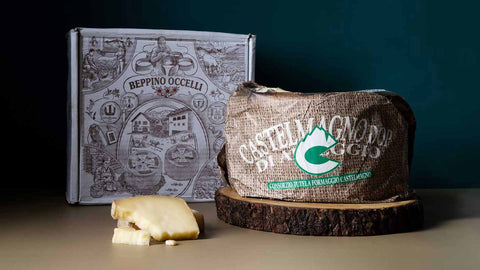 A wheel of Castelmagno DOP Cheese on top of a round wood board with a white Beppino Occelli box on the side and a slice of cheese in front. 