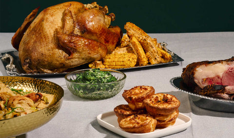 A whole roasted turkey with a side of corn ribs, yorkshire pudding, creamed spinach. On the side, is a prime rib peaking. 