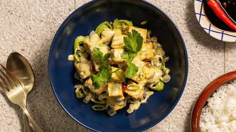 A photo of sisig tofu in a blue bowl at the center, gold spoon and fork, white rice, and red peppers on the side