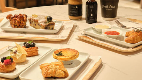A table filled with Joel's Place treats like bread, pastries, and coffee