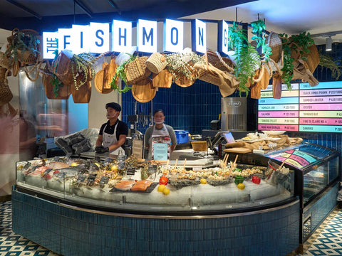 Two attendants behind a display case featuring various seafood on ice at The Fishmonger section at Joel's Place Glorietta 4