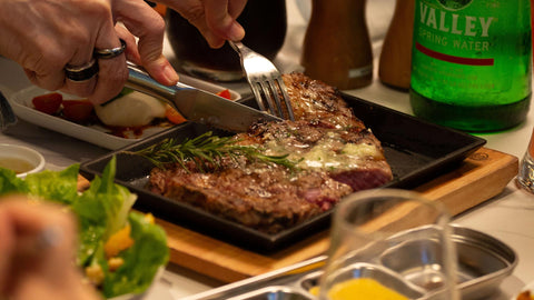 a person holding a fork and knife slicing a well-done steak