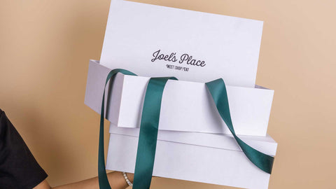 A person on the side holding a stack of white Joel's Place boxes with green ribbon. 