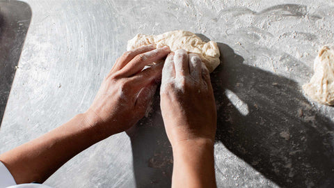 Hands folding dough on a floured metal surface
