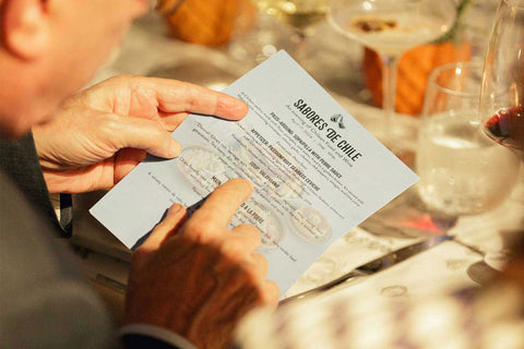 A man sitting at a dining table reading the Cocina de Chile event menu at Joel's Place