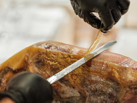 A photo of hand slicing a cured Iberian pork thinly