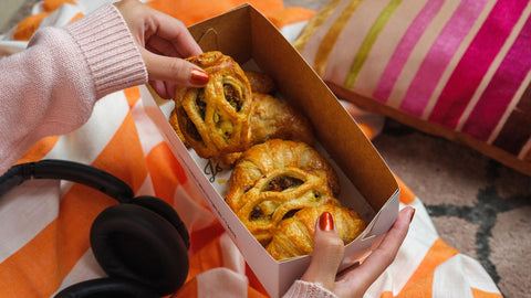 A person picking a flaky pastry from a Joel's Place box during a cozy rainy day at home, ideal feel-good food for gloomy days.