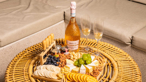 An angled shot of a beautifully arranged charcuterie board with sparkling rosé wine, cheese, snacks, muscat grapes, and two champagne flutes, curated for Mother’s Day themed gift bundles using Joel’s Place products.