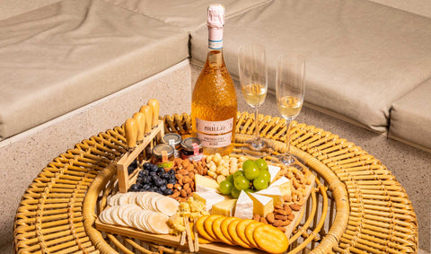An angled shot of a beautifully arranged charcuterie board with sparkling rosé wine, cheese, snacks, muscat grapes, and two champagne flutes, curated for Mother’s Day themed gift bundles using Joel’s Place products.