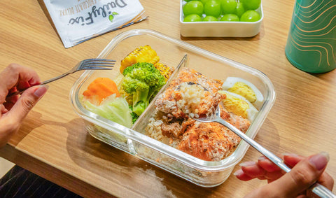 a packed lunch on top of a table with a person holding a spoon and fork