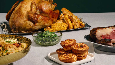 A whole roasted turkey with a side of corn ribs, yorkshire pudding, creamed spinach. On the side, is a prime rib peaking. 