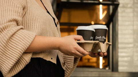 A close-up shot of a person holding two cups of coffee purchased from the Bakery Window at Joel’s Place