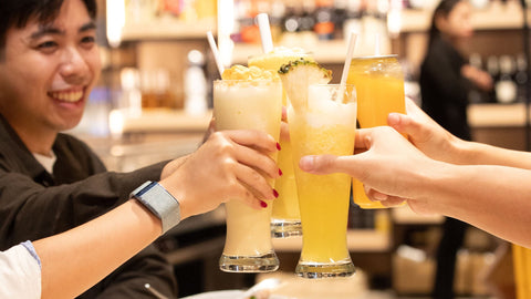 A group of people seated in an indoor dining area with a table toasting with drinks at Joel's Place—a self‑service Grocerant