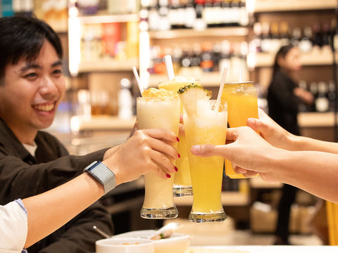 A group of people seated in an indoor dining area with a table toasting with drinks at Joel's Place—a self‑service Grocerant