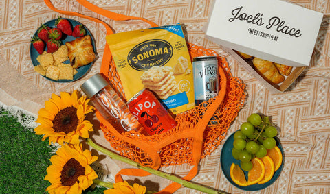 An outdoor picnic spread featuring Joel’s Place favorites—bakery items, ready-to-eat meals, gourmet snacks, and beverages.