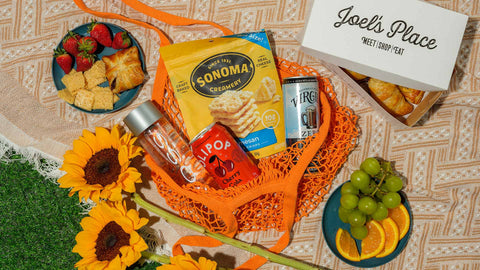 An outdoor picnic spread featuring Joel’s Place favorites—bakery items, ready-to-eat meals, gourmet snacks, and beverages.