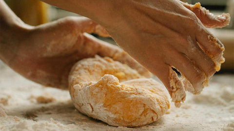 A close-up of hands kneading dough on a floured surface made by hand. 