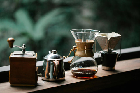 A photo of neatly arranged set of pour-over coffee tools lined up on a countertop, with a n outdoor background filled with greenery and plants