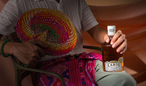 A man sitting on a chair holding an abanico fan and a bottle of Kanto Vodka