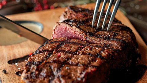 This image shows a perfectly seared, juicy grilled steak being sliced on a wooden serving board.