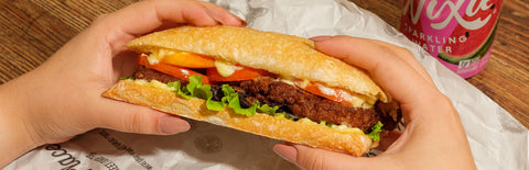 A close up image of hands holding a grilled chorizo patty sandwich from Joel's Place