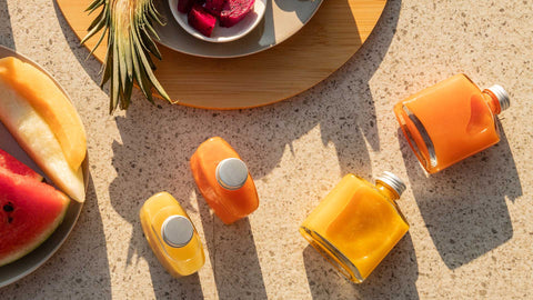 A photo of an overhead view of a sunny poolside with fresh tropical fruits, alongside bottles of Joel's Place Powershot juices