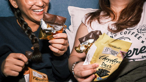 Two girls laughing and eating two Chocolove chocolates while sitting in bed