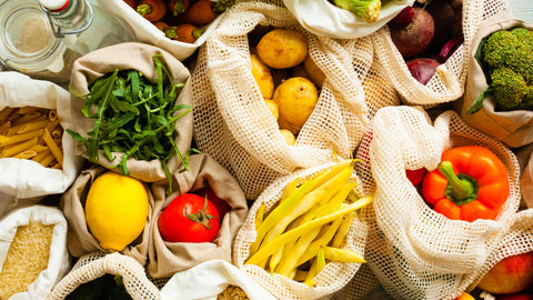 A wide shot of a variety of fresh produce, including fruits, vegetables, and other pantry staples stored in reusable textile bags and glass jars, highlighting seasonal ingredients from Joel’s Place.