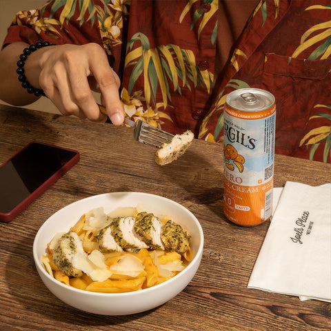Man eating a bowl of Creamy Pesto Rosso pasta, a warm and filling comfort food pick for rainy days, accompanied by a beverage available at Joel's Place.