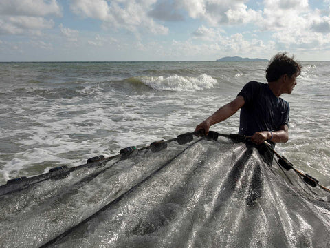 A fisherman standing in the sea pulling a fishing net