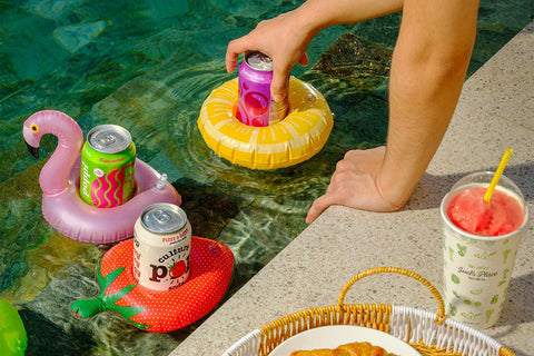 A person's hand reaching towards a swimming pool with refreshing flavored drinks from the Grocer in inflatable floaties—available via Click and Collect at Joel’s Place Makati