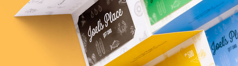 An image of multiple gift cards from Joel’s Place displayed within colorful, folded paper packaging that can be used to purchase any of the products in-store. 