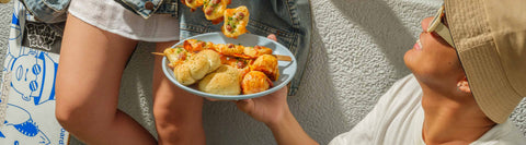 Two individuals enjoying a casual outdoor gathering with beverages, sausage rolls, and bread from Joel’s Place Special Orders during a skate break hangout.