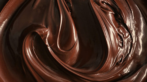 A close-up image of chocolate ganache swirls, showcasing its rich, dark brown color and smooth, glossy texture, featuring a thick, viscous consistency.  