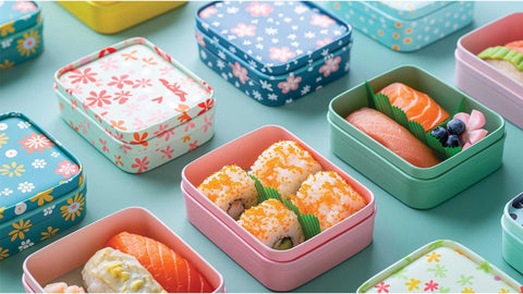 Perfectly lined square lunch boxes in different patterned designs with an assortment of sushi and maki rolls inside. 